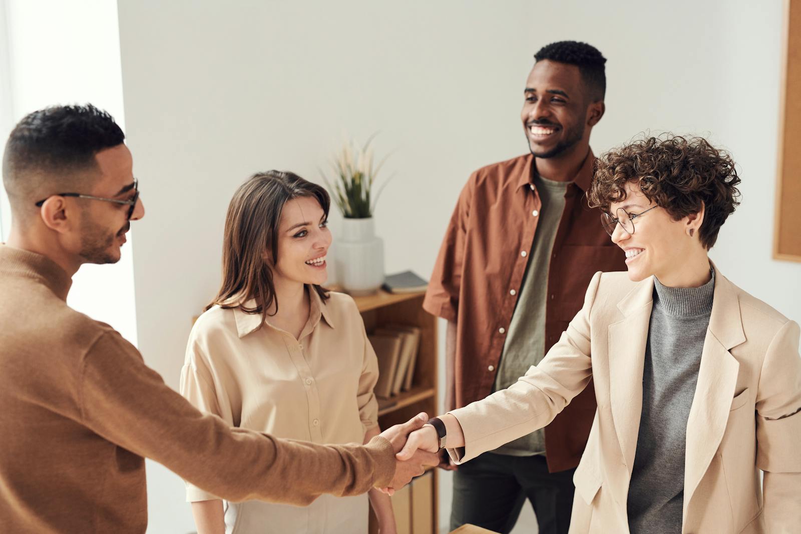Four colleagues smiling and shaking hands in a bright office setting. small business consultant