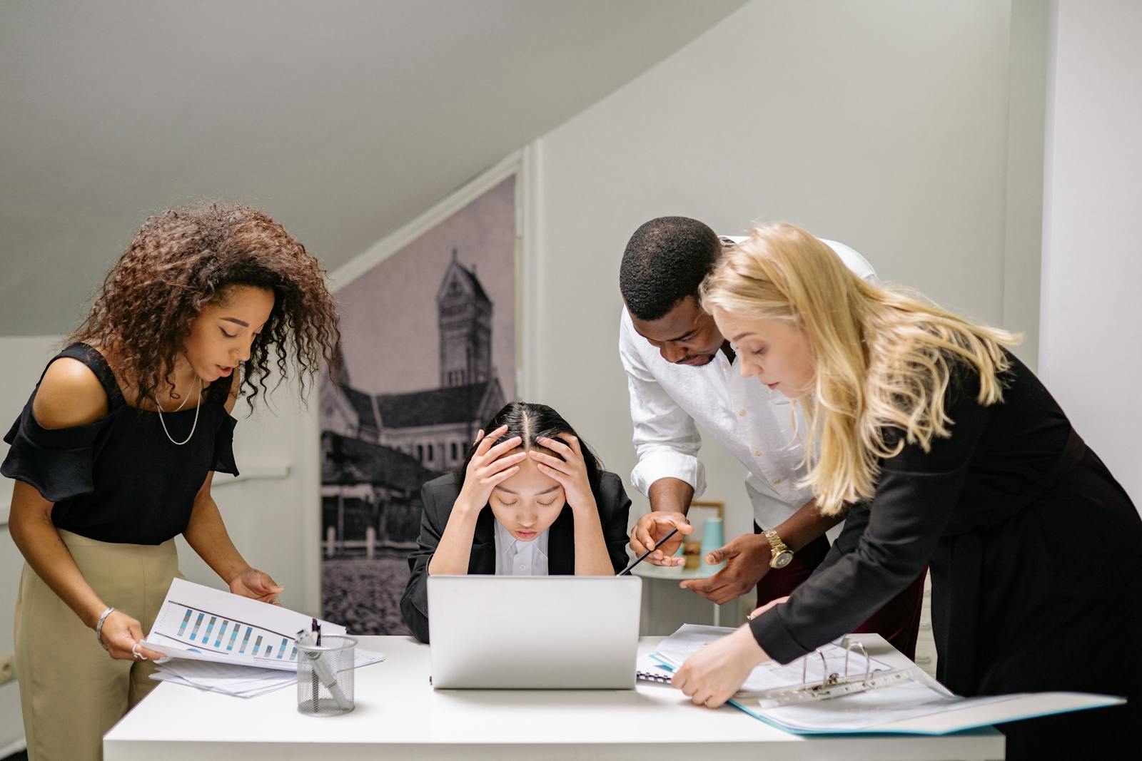 Diverse group of coworkers engaged in a collaborative office meeting, discussing around a laptop. what does a social media manager do